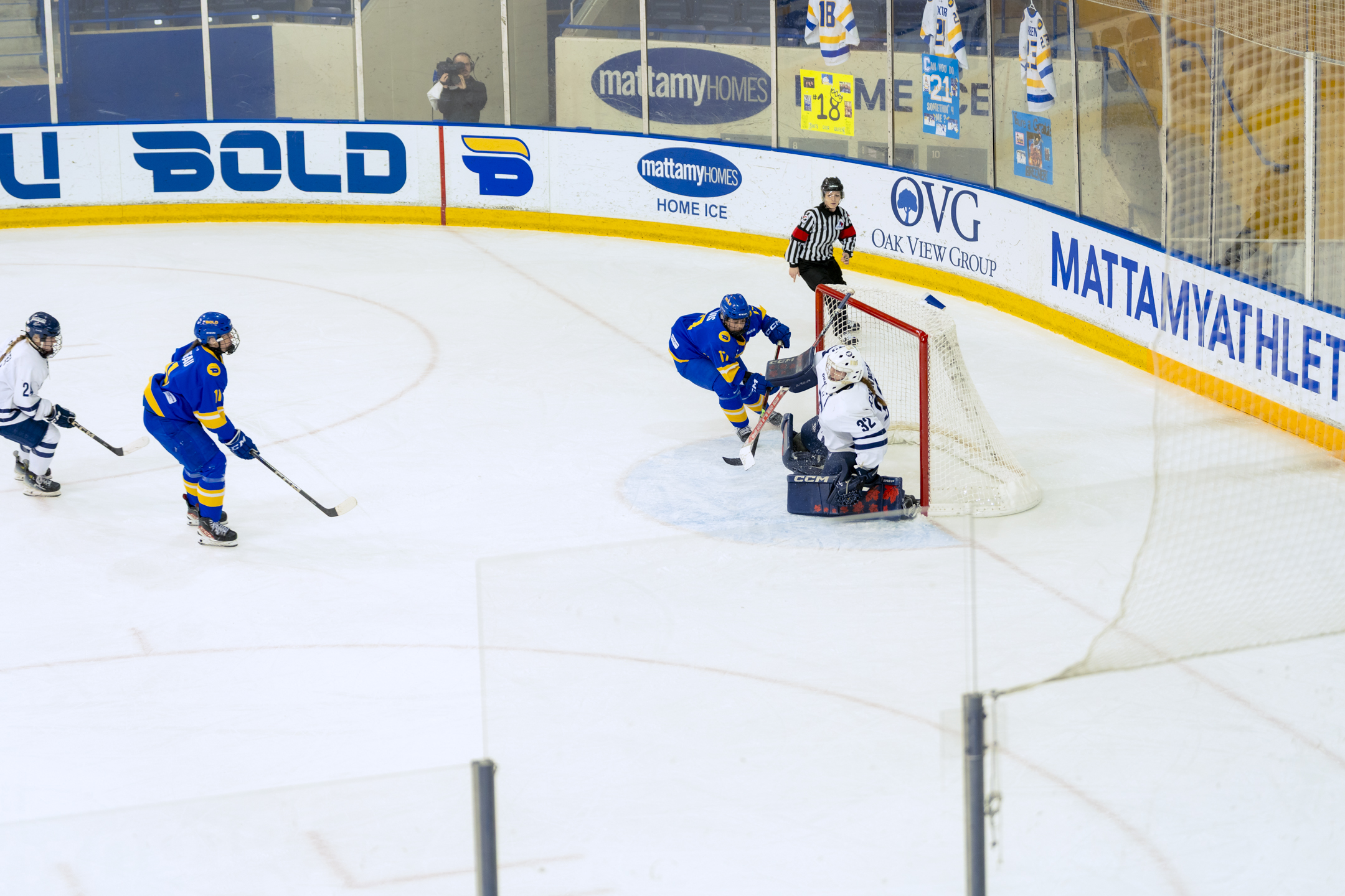 A TMU Bold women's hockey player attempts to tap a puck into the net behind U of T's goalie